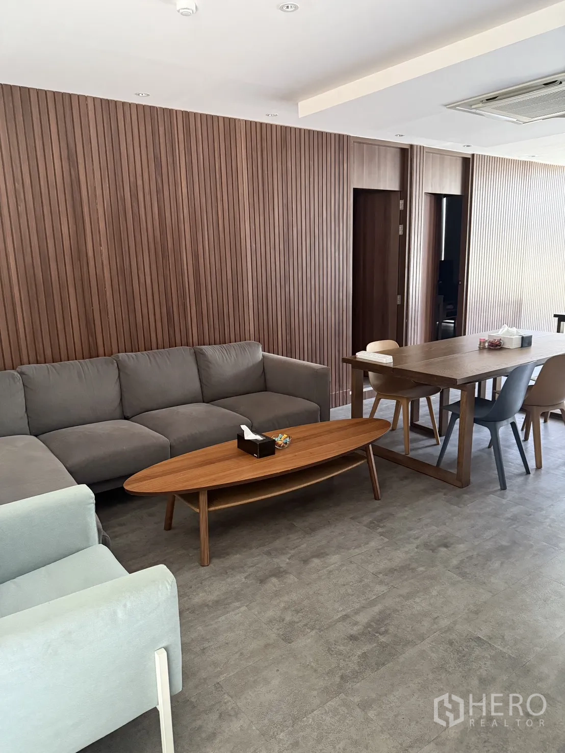 โฮมออฟฟิศ for rent in Watthana, Bangkok - โซนรับรองพร้อมโซฟาสีเทา โต๊ะกาแฟไม้ และโต๊ะทำงาน-ประชุม ผนังลายไม้