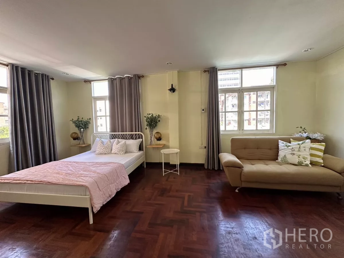 Home Office for rent in Suan Luang, Bangkok - Spacious corner bedroom with sofa, multiple windows, and parquet floor.