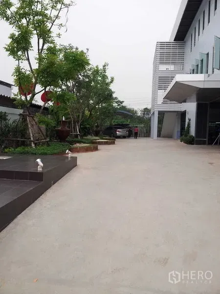 Warehouse for rent or sale in Bang Phli, Samut Prakan - Wide concrete driveway and landscaped entry area beside the warehouse building.