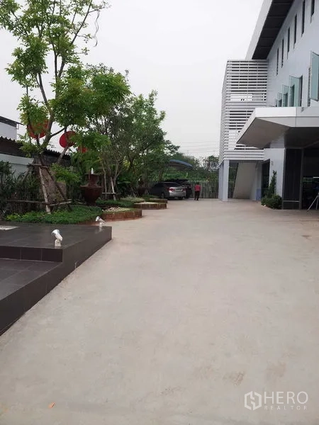 Warehouse for rent or sale in Bang Phli, Samut Prakan - Wide concrete driveway and landscaped entry area beside the warehouse building.