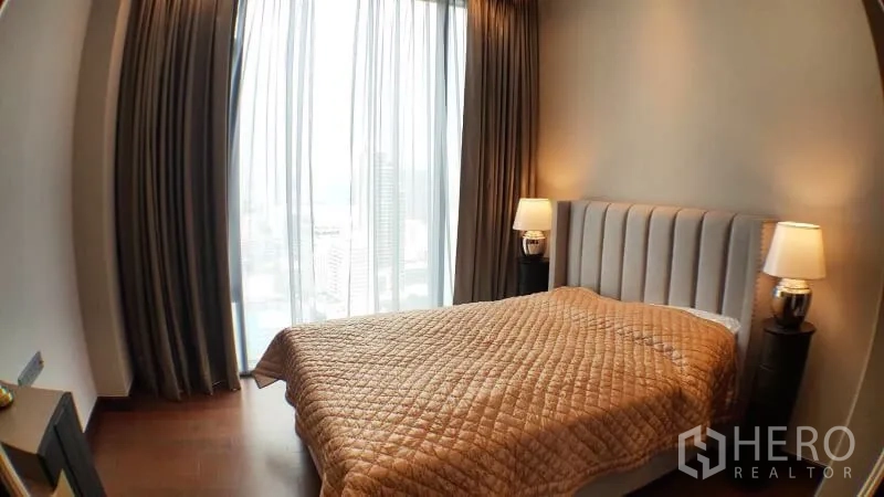 Condominium for rent in Khlong Toei, Bangkok - Bedroom with large windows, city view and bedside lamps.