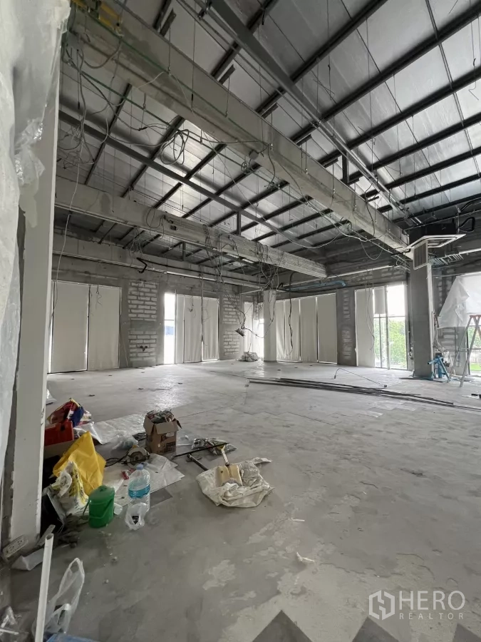 Retail Space for rent in Khlong Toei, Bangkok - Unfinished retail space showing exposed beams, wiring and multiple windows with construction materials on the floor.