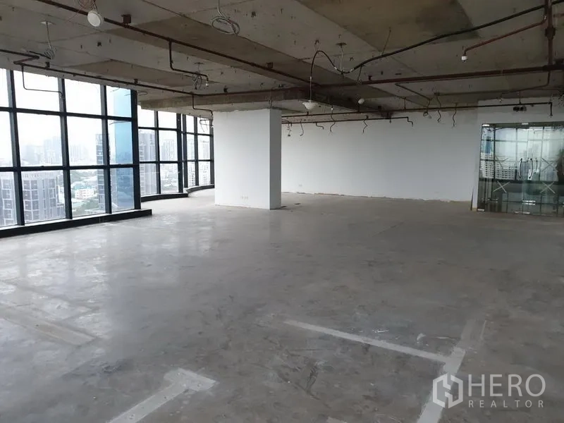 Office Space for rent in Watthana, Bangkok - Large unfinished office with exposed ceiling, glass entry doors, and wraparound windows.
