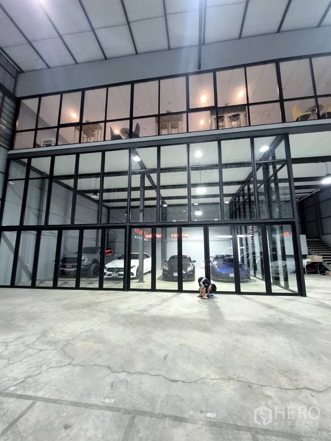 Warehouse for rent in Sai Mai, Bangkok - Ground-level glass bays with parked vehicles beneath mezzanine offices.