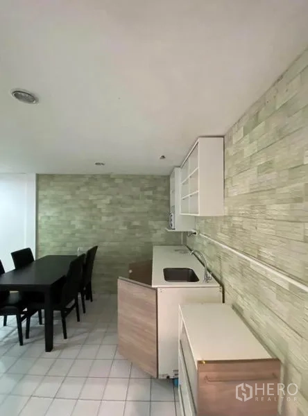 Townhouse for rent in Khlong Toei, Bangkok - Compact kitchen and dining area with stone-textured backsplash and white cabinetry.
