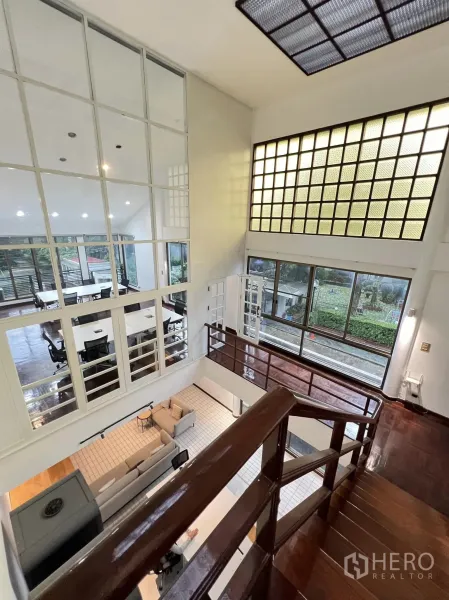 Townhouse for rent in Watthana, Bangkok - Double-height living area with mezzanine, glass-block wall, and polished wood stairs.
