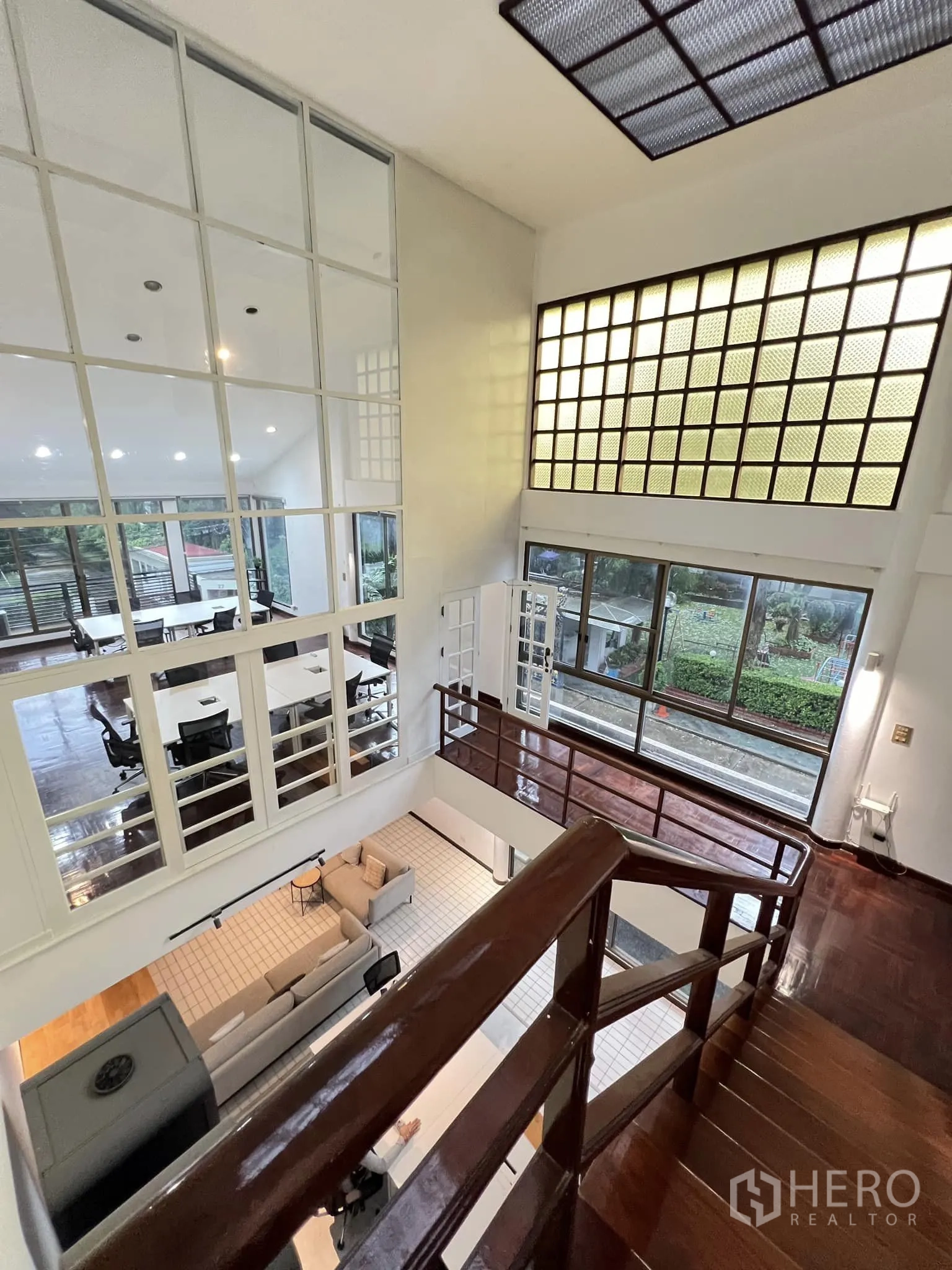 Townhouse for rent in Watthana, Bangkok - Double-height living area with mezzanine, glass-block wall, and polished wood stairs.