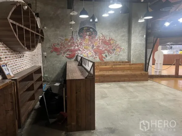 零售空间 出租在Khlong Toei, Bangkok - 室内混凝土地面，木架与吧台，砖墙及彩色墙绘，吊灯照明。