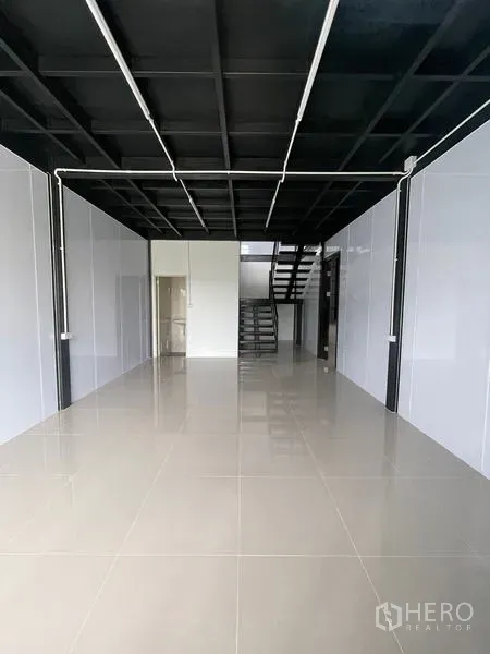 Warehouse for rent in Lam Luk Ka, Pathum Thani - Ground-floor office or showroom with glossy tile floors, high black ceiling and a staircase at the back.