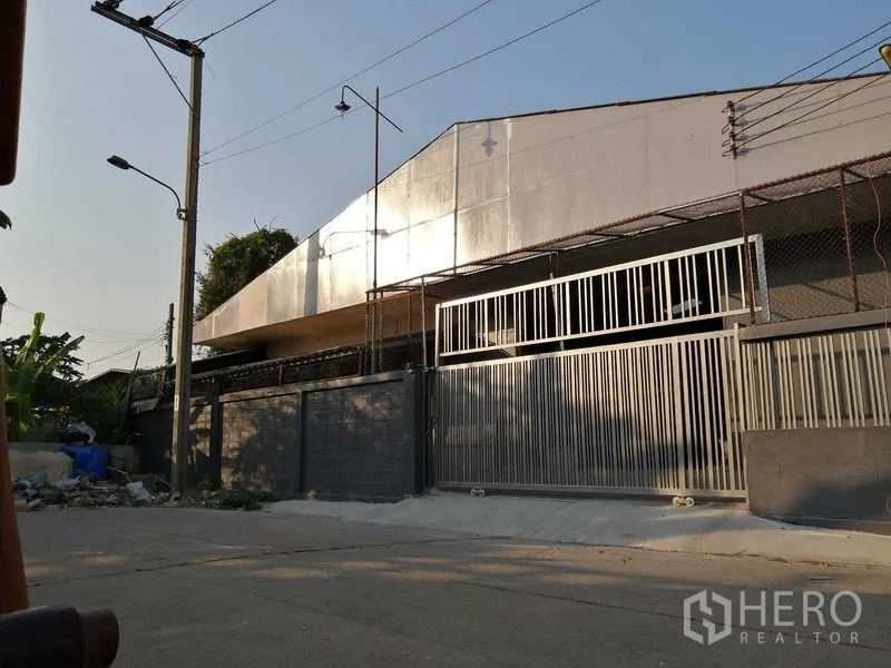 货栈 出租在Nonthaburi - 仓库外观，临街高金属滑动门与围栏。