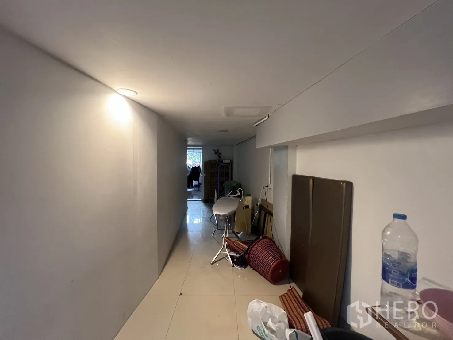 Retail Space for rent - Long interior hallway with low ceiling, glossy tiles and storage items along the wall.
