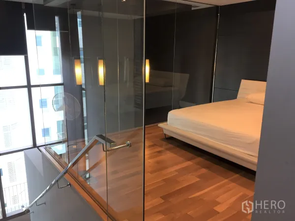 Condominium for rent in Khlong Toei, Bangkok - Loft-style bedroom on a mezzanine with glass walls, wood flooring, pendant lights and large windows.