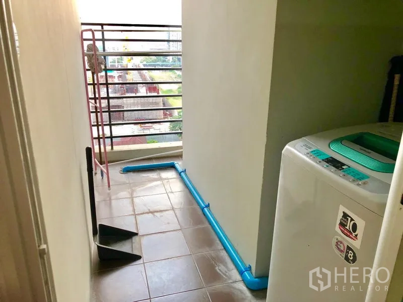 Condominium for rent in Huai Khwang, Bangkok - Utility balcony with washing machine, tiled floor, and metal railing overlooking the city.