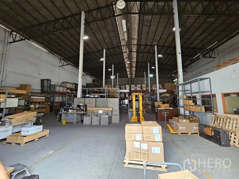 货栈 出租在Khlong Toei, Bangkok - 宽阔通道的仓库，托盘与纸箱整齐摆放，配高架货架与高棚照明。