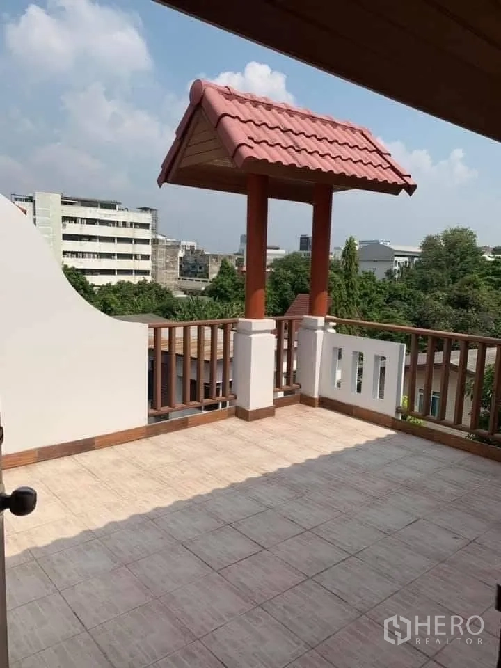 Townhouse for rent in Watthana, Bangkok - Rooftop terrace with tiled floor, wooden railing, a small red-tile roof and city views.
