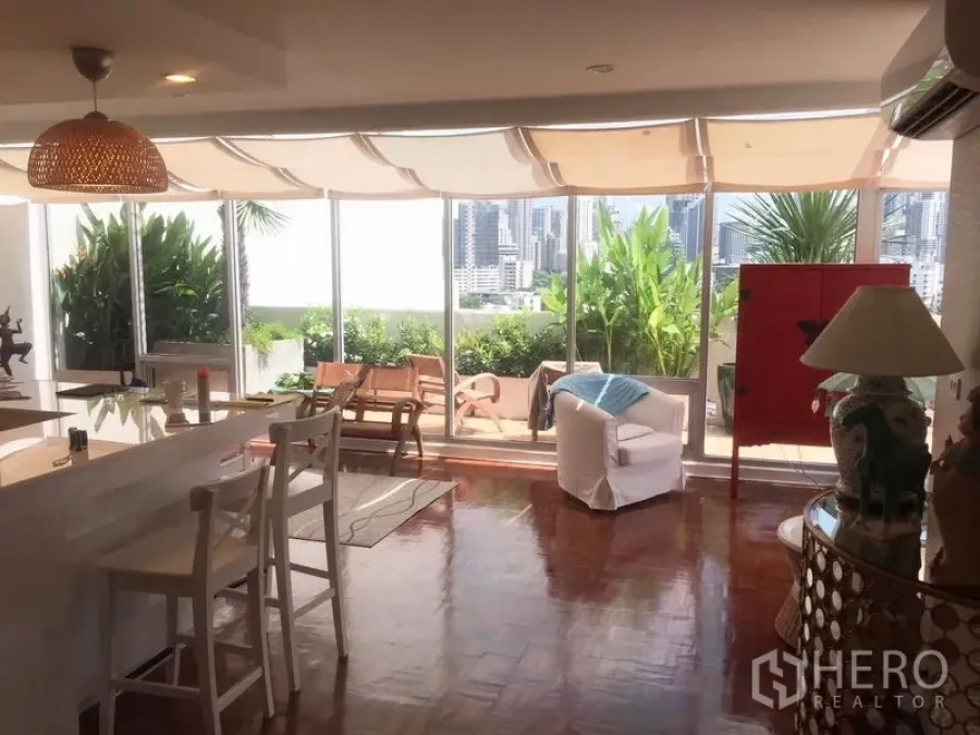 Condominium for rent in Khlong Toei, Bangkok - Bright open-plan living room with floor-to-ceiling windows opening to a lush terrace and Bangkok skyline views.