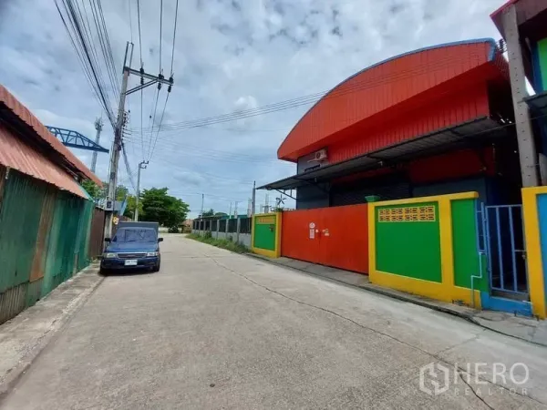 Warehouse for rent or sale in Bang Bua Thong, Nonthaburi - Quiet industrial street in Bang Bua Thong showing warehouse frontage and roadside parking.