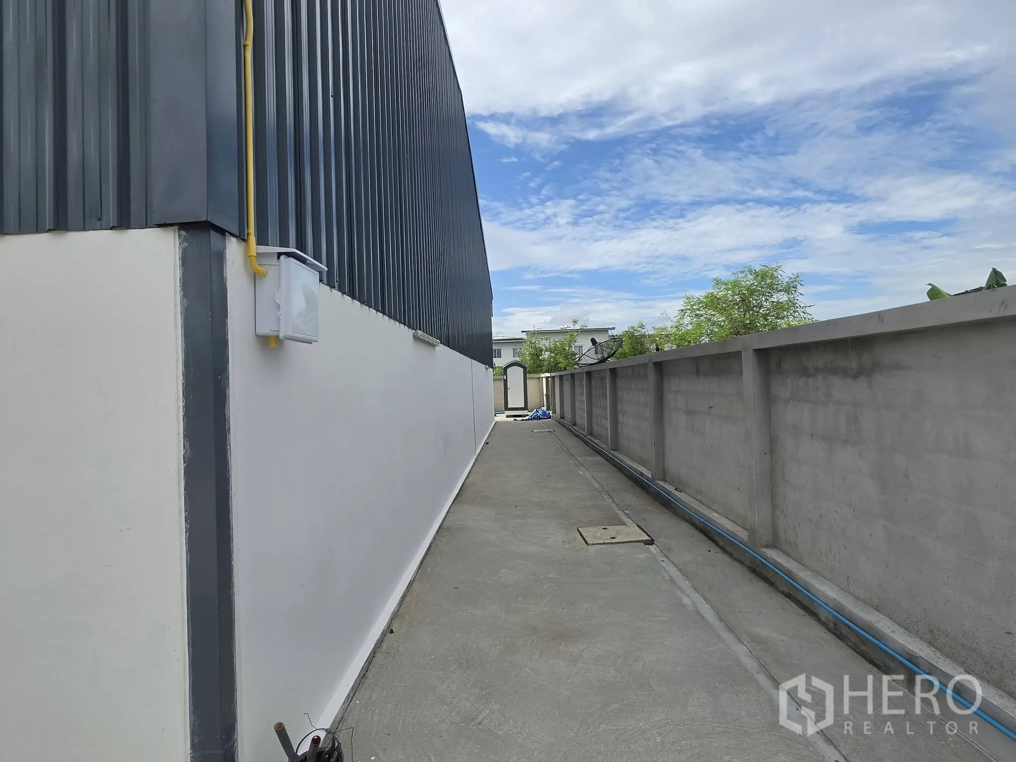 Warehouse for rent in Mueang Samut Prakan, Samut Prakan - Side passage along the warehouse with perimeter wall and visible utility conduits.