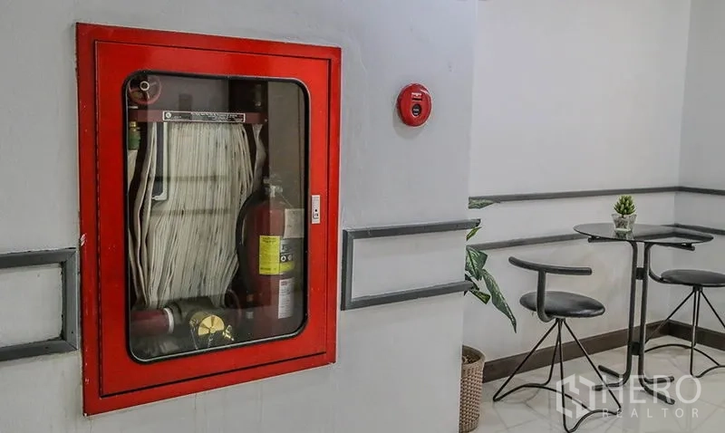 Office Space for rent in Bang Na, Bangkok - Corridor corner featuring a red fire hose cabinet and extinguisher beside a small seating area.