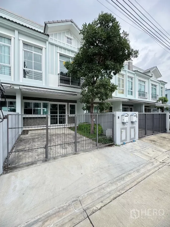 Townhouse for rent in Prawet, Bangkok - Modern townhouse facade with gated driveway and a tree-lined front yard.