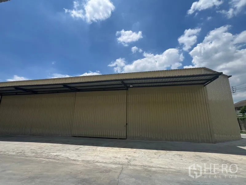 Warehouse for rent in Phra Khanong, Bangkok - Panoramic exterior of the metal warehouse with long facade, awning, and wide driveway.