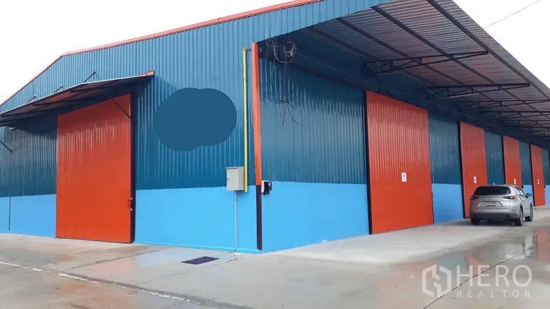 Factory for rent in Khlong Luang, Pathum Thani - Close exterior of multiple factory shutters beneath a long canopy with parking area in front.