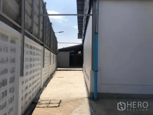 Warehouse for rent in Prawet, Bangkok - Concrete side passage beside the warehouse with boundary wall and blue drainpipe.