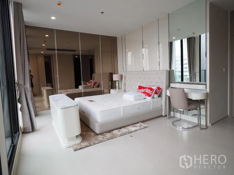 Condominium for rent in Pathum Wan, Bangkok - Large bedroom with neutral tones, mirrored closets, vanity station and wide windows.
