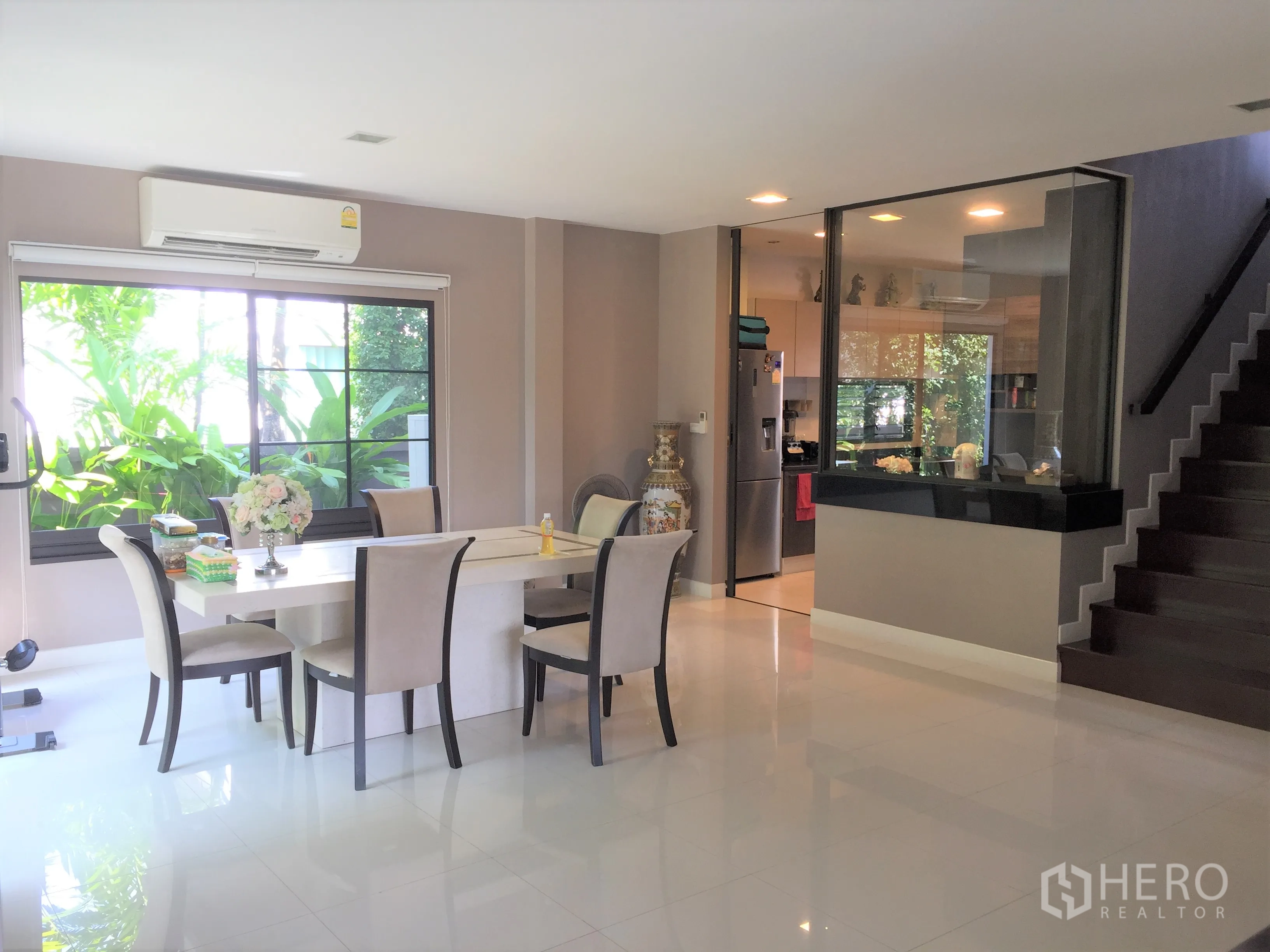 Detached House for rent or sale in Prawet, Bangkok - Dining space next to a glass-partitioned kitchen and staircase, with air conditioning and picture windows.