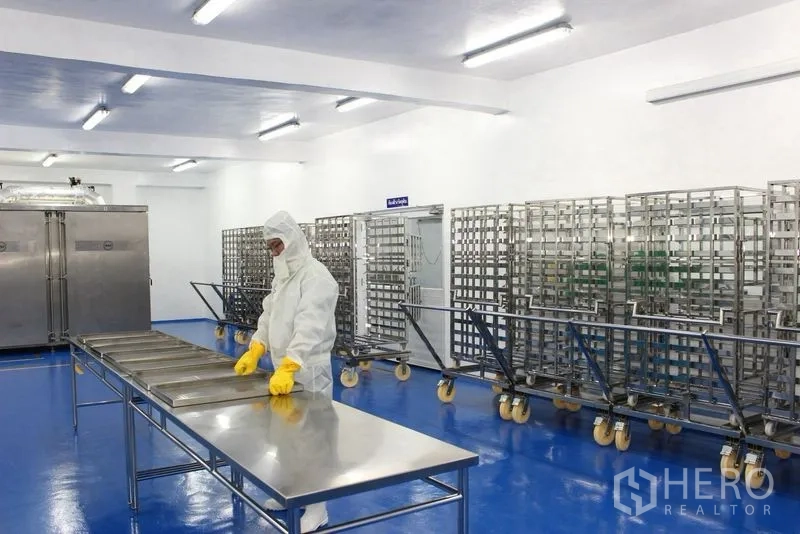 Factory for rent or sale in Krathum Baen, Samut Sakhon - Sterile workspace with stainless tables and rows of wheeled metal racks beside chambers.
