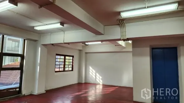 Office Space for rent or sale in Khlong Toei, Bangkok - Open-plan office with red floor, large windows, and overhead fluorescent lights.
