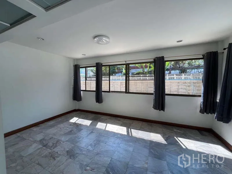 Detached House for rent in Bang Na, Bangkok - Spacious room with long windows, gray curtains and stone-pattern floor tiles.