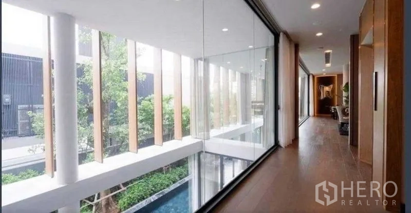 Detached House for sale in Huai Khwang, Bangkok - Upper walkway with floor-to-ceiling glass overlooking the courtyard pool and trees.