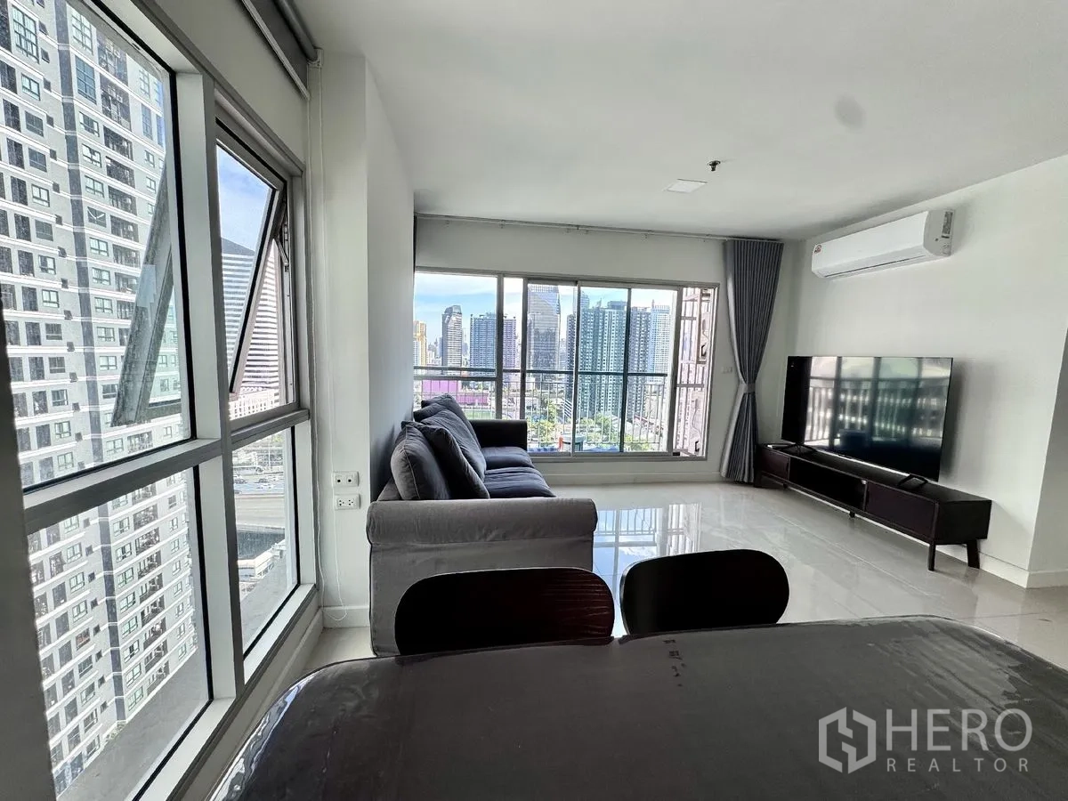 คอนโด for rent in Huai Khwang, Bangkok - ห้องนั่งเล่นสว่างด้วยหน้าต่างบานใหญ่ โซฟาสีเทา ชั้นวางทีวี และวิวเมือง
