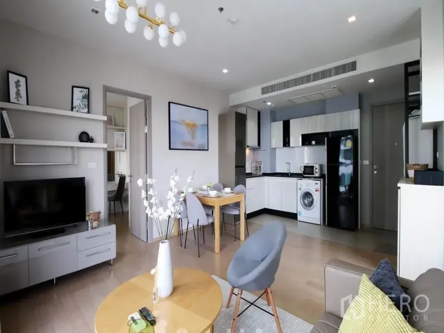 Condominium for rent or sale in Khlong Toei, Bangkok - Modern open-plan living, dining and kitchenette with washing machine and TV unit in a bright condo.