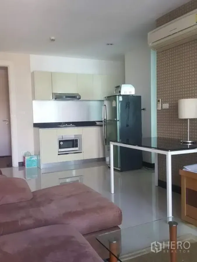 Condominium for rent in Khlong Toei, Bangkok - Open-plan living room with brown sofa, compact built-in kitchen, stainless refrigerator, and dining table.