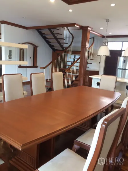 Detached House for rent in Khlong Toei, Bangkok - Large solid-wood dining table with upholstered chairs beside the staircase.