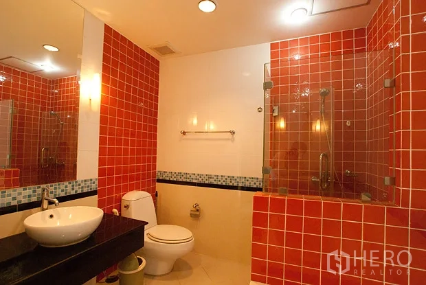 Condominium for rent in Khlong Toei, Bangkok - Modern bathroom with red mosaic tiles, glass-enclosed shower, vanity and toilet.