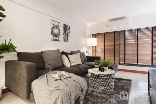 Townhouse for rent in Khlong Toei, Bangkok - Cozy living room with sectional sofa, coffee table, and large blinds.