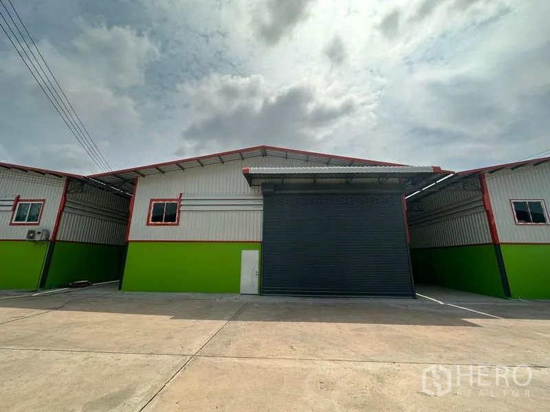Warehouse for rent in Khlong Toei, Bangkok - Modern warehouse exterior with roll-up shutter door, side access door, and driveway parking.