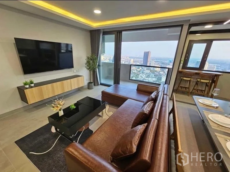 Condominium for rent or sale - Living area with wall-mounted TV, sectional sofa and balcony outlook.