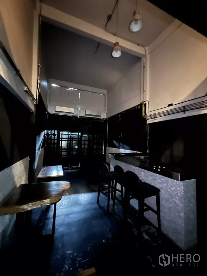 店屋 出租在Watthana, Bangkok - 一层室内高挑空间，吊灯、吧台与木桌，面向前方栅栏门。