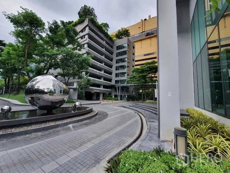 Condominium for sale in Khlong Toei, Bangkok - Condominium entrance with landscaped driveway, water feature, and silver sphere sculpture.