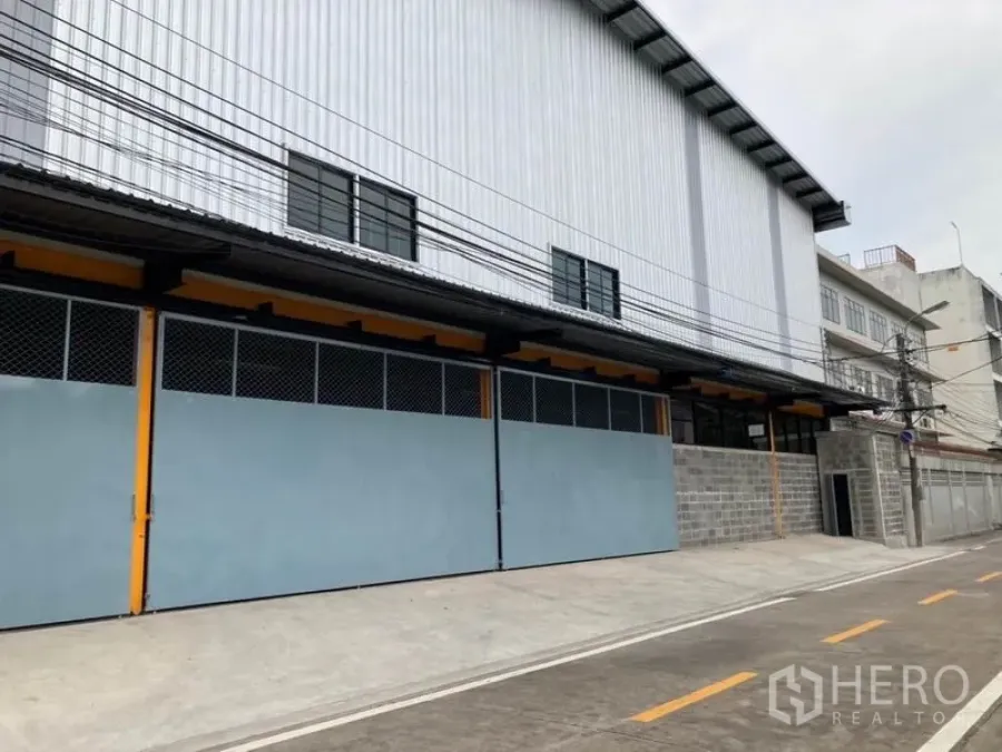 Warehouse for rent in Khlong Toei, Bangkok - Modern warehouse exterior with long sliding steel gates and corrugated metal facade on a quiet industrial lane in Bangkok.