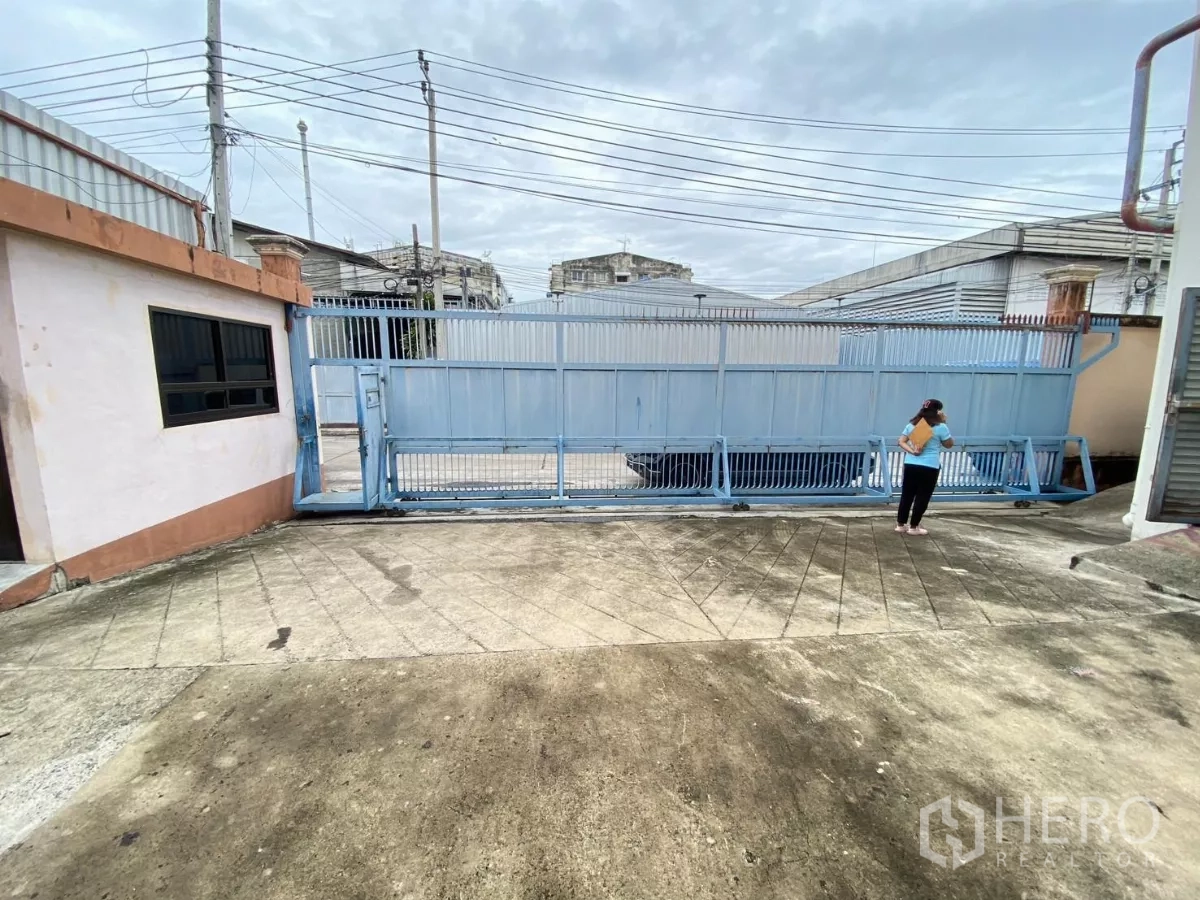 Factory for rent in Khlong Toei, Bangkok - Secure sliding gate and concrete driveway at the factory entrance.