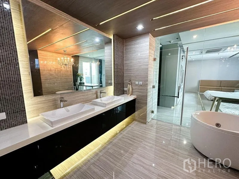 Condominium for rent or sale in Khlong Toei, Bangkok - Bathroom featuring a double vanity, large mirror and glass door to the suite.