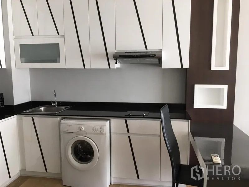 Condominium for rent in Bangkok - Compact modern kitchen with white striped cabinets, black countertops, hob, range hood and front-loading washer.