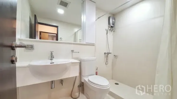 Condominium for rent in Khlong Toei, Bangkok - Modern white bathroom featuring a wall-mounted sink, toilet and walk-in shower with water heater.