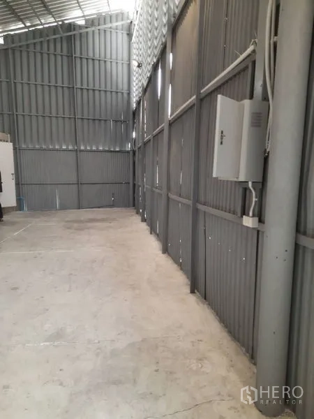 Warehouse for rent in Sathon, Bangkok - Warehouse side aisle showing electrical panel, conduits and corrugated steel walls.