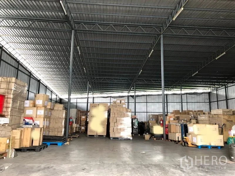 Warehouse for rent in Pak Kret, Nonthaburi - Spacious warehouse interior with steel columns, concrete floor and stacked pallets of boxes.